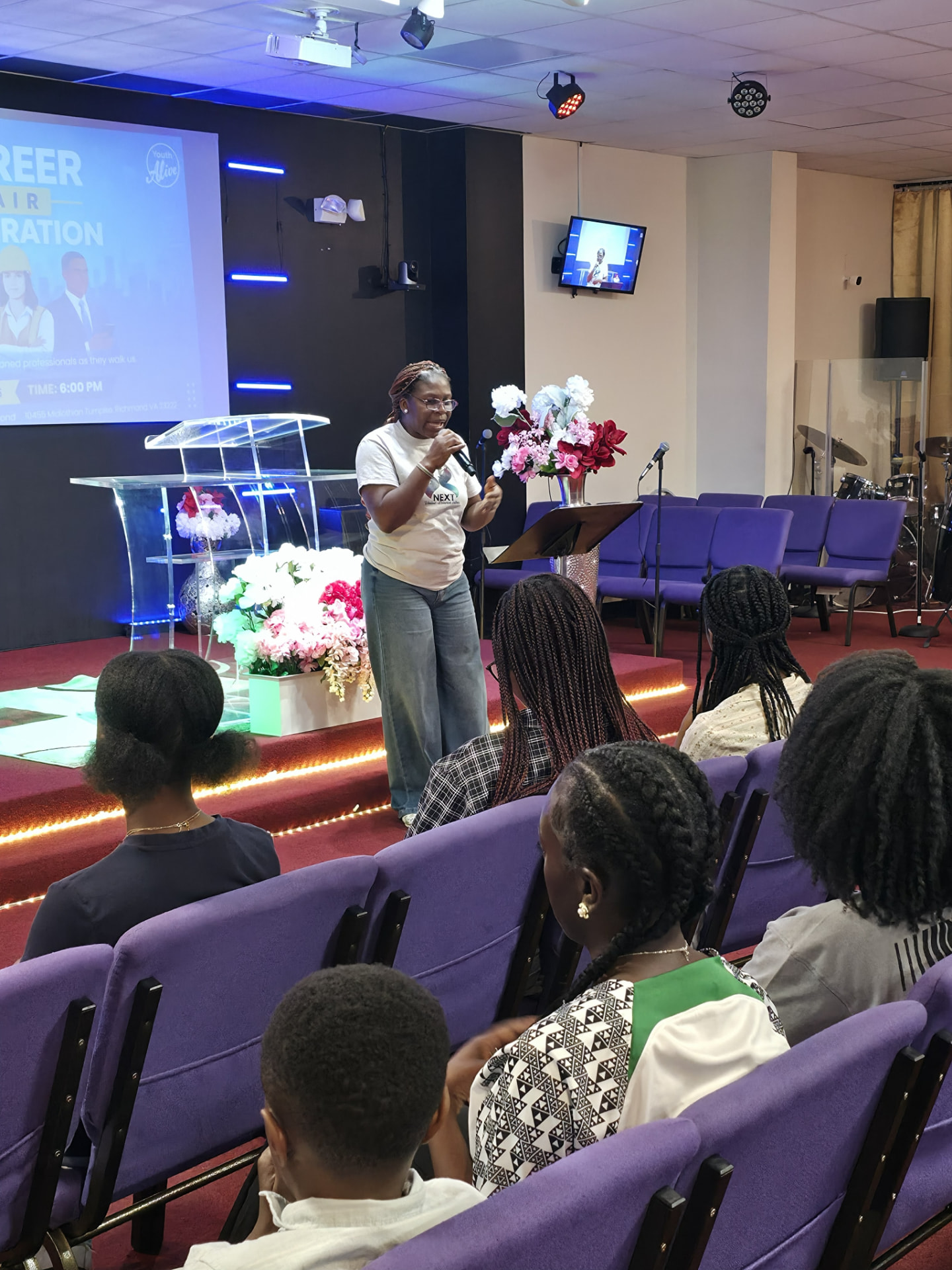 Aunty Kemi speaking with a microphone at a NEXT Academy career night